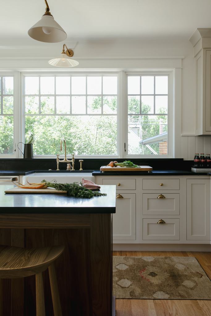 Modern kitchen with a black countertop, white cabinetry, a wooden island, and a view of greenery through large windows.